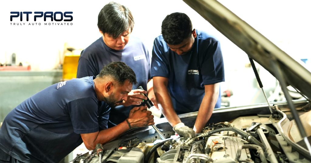 Three Pitpros technicians working together under the hood of a car during an engine inspection at a Dubai auto service center.