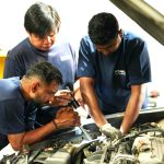 Three Pitpros technicians working together under the hood of a car during an engine inspection at a Dubai auto service center.