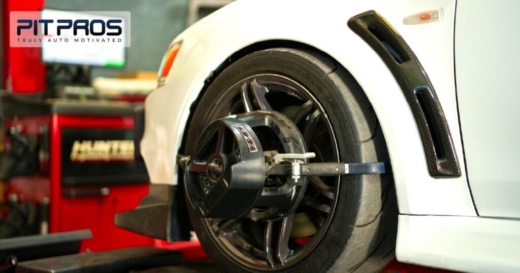“Close-up of a car undergoing wheel alignment at a professional auto service center, with alignment equipment attached to the wheel and Pit Pros branding visible.”
