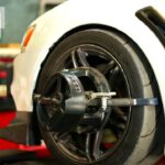 “Close-up of a car undergoing wheel alignment at a professional auto service center, with alignment equipment attached to the wheel and Pit Pros branding visible.”